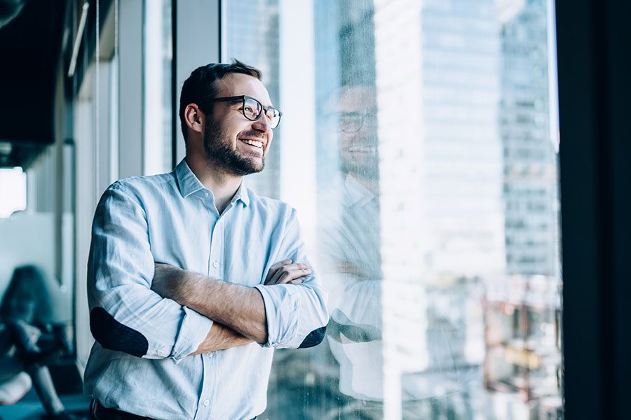 Business Insurance - Portrait of a Smiling Businessman Looking Out the Window from His Office