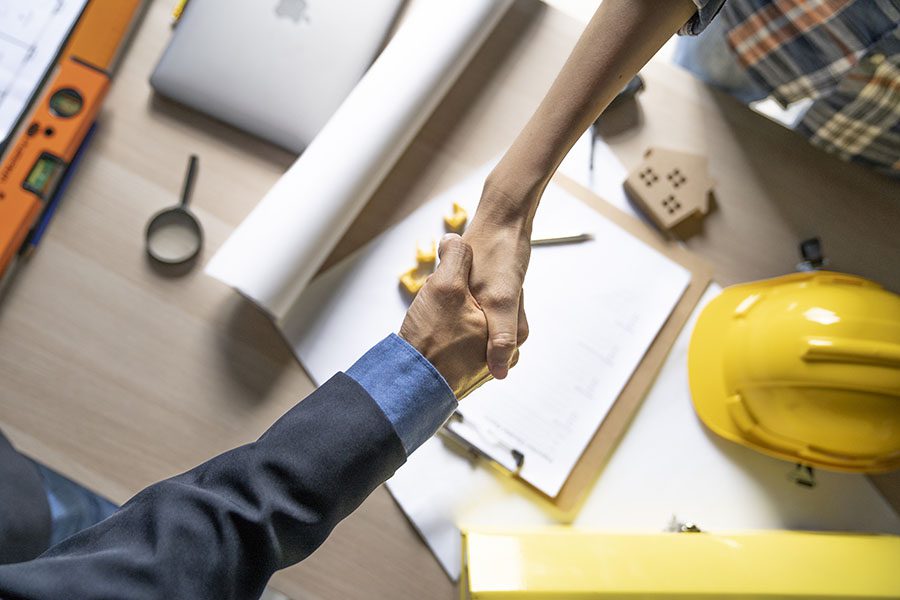 Specialized Business Insurance - Contractor and Businessman Shaking Hands Across Wooden Table with New Construction Blueprints